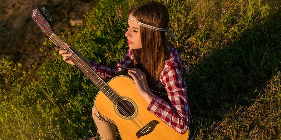 a woman with long brown straight hair sitting on green grass while holding an acoustic guitar